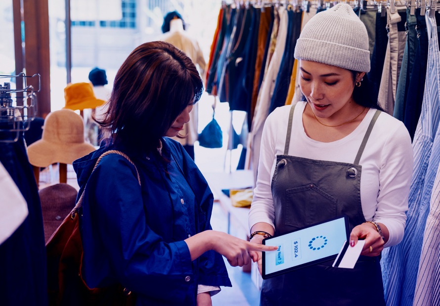 Two retail workers review sales data on a tablet in a clothing store